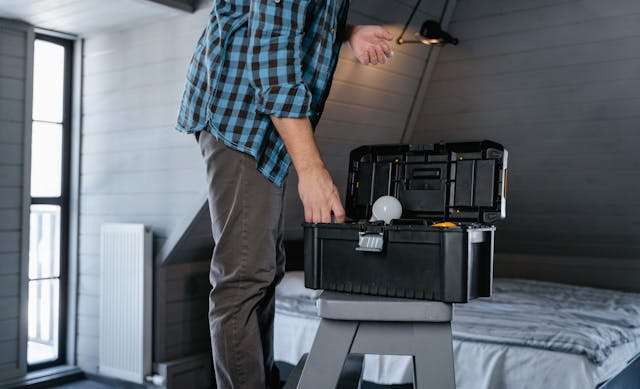 someone on a stepladder reaching into a black toolbox and changing a lightbulb